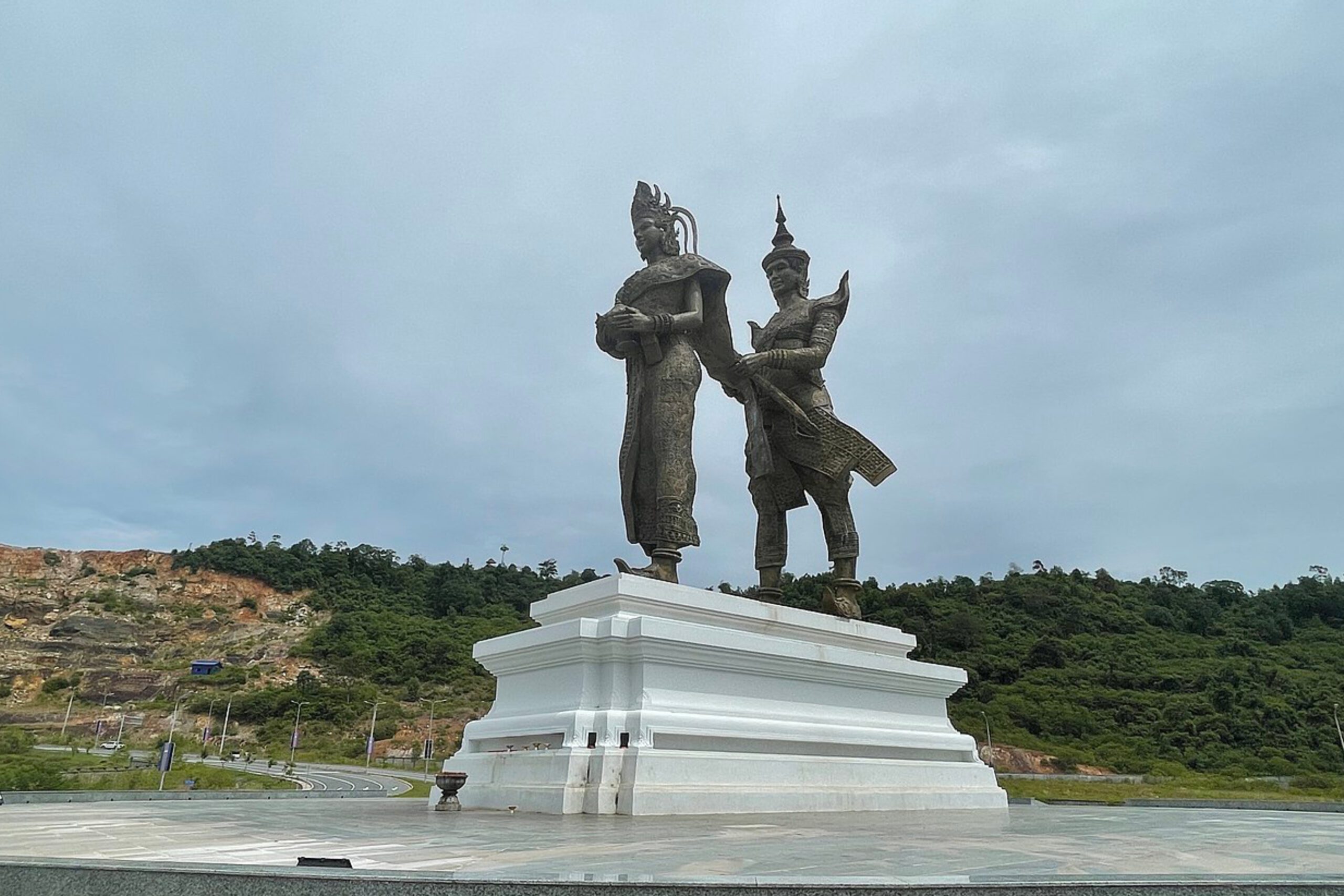 Monument featuring the statues of Preah Thong and Neang Neak on a white pedestal, surrounded by green hills, marking a cultural landmark in Sihanoukville, Cambodia.